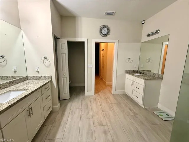 Spacious bathroom featuring two vanity areas with granite countertops, integrated sinks, white cabinetry, and large wall-mounted mirrors
