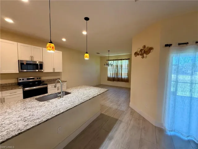 Open-concept kitchen featuring white cabinetry, stainless steel appliances, a large island with sink, and recessed lighting