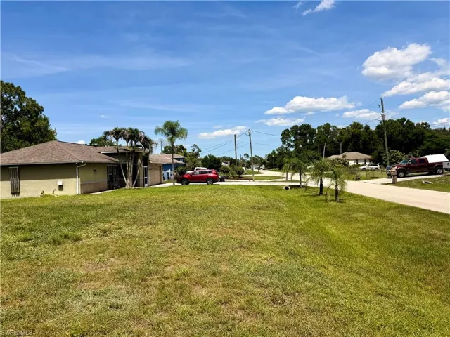 Expansive grass lot featuring a paved road, mature trees, and a clear sky