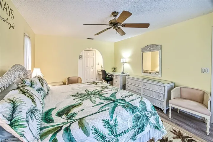 Bedroom with a ceiling fan, wood finished floors, arched walkways, and a textured ceiling
