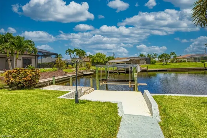Dock featuring boat lift, a yard, a water view, and a residential view