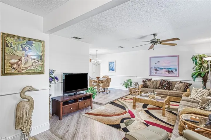 Living area featuring a textured ceiling, light wood-type flooring, ceiling fan, and suspended lighting