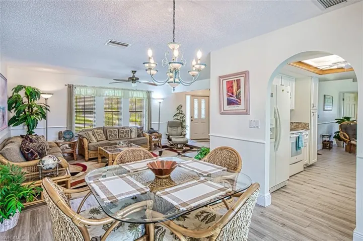Dining room with arched walkways, hanging lights, a textured ceiling, light wood-style flooring, and ceiling fan
