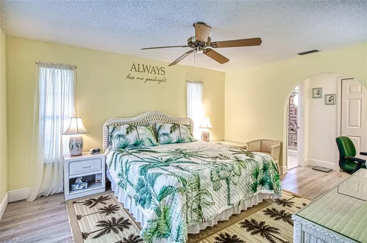 Bedroom with arched walkways, a textured ceiling, a ceiling fan, and light wood-style flooring