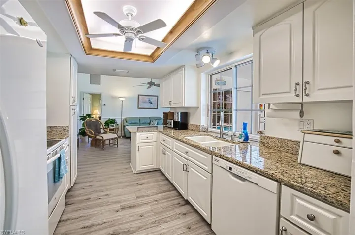 Kitchen with white appliances, white cabinets, light stone counters, a tray ceiling, and light wood-type flooring