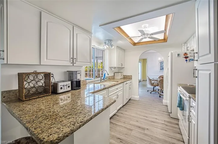 Kitchen featuring a raised ceiling, white cabinets, arched walkways, white appliances, and light stone counters
