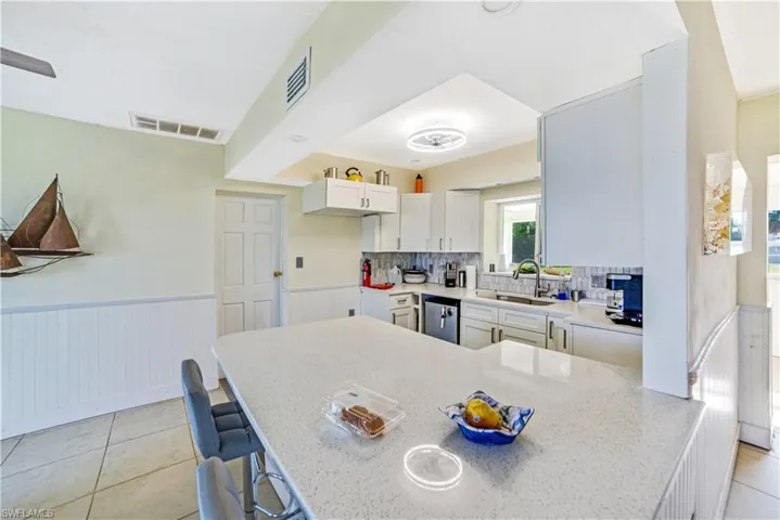Kitchen featuring a breakfast bar, sink, white cabinetry, stainless steel dishwasher, and kitchen peninsula