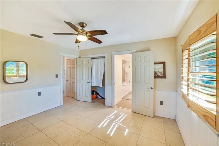 Unfurnished bedroom featuring light tile patterned floors, ceiling fan, and ensuite bath
