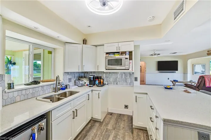 Kitchen featuring dark wood-type flooring, sink, dishwasher, decorative backsplash, and white cabinets