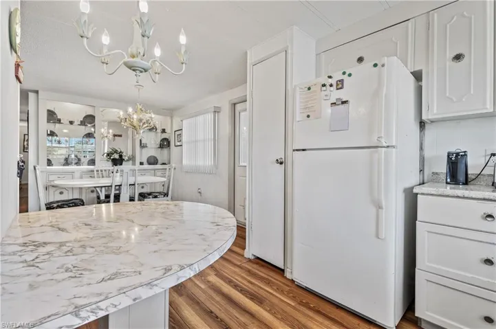 Kitchen with white cabinetry, freestanding refrigerator, dark wood-style floors, suspended lighting, and light stone countertops