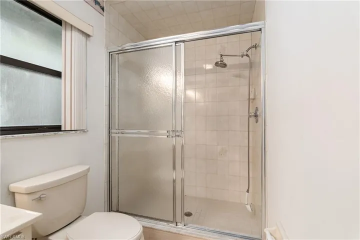 Bathroom featuring a shower with door, toilet, and vanity