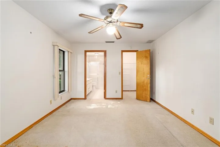 Unfurnished bedroom featuring a walk in closet, light colored carpet, ensuite bathroom, and ceiling fan