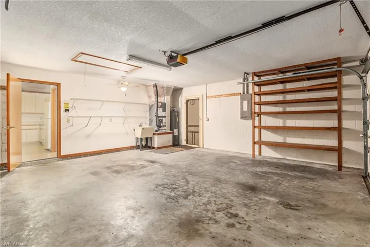 Garage with heating unit, water heater, sink, a garage door opener, and electric panel