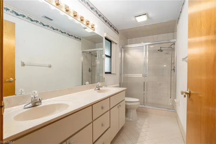 Bathroom featuring a shower with door, a textured ceiling, tile patterned floors, toilet, and double sink vanity