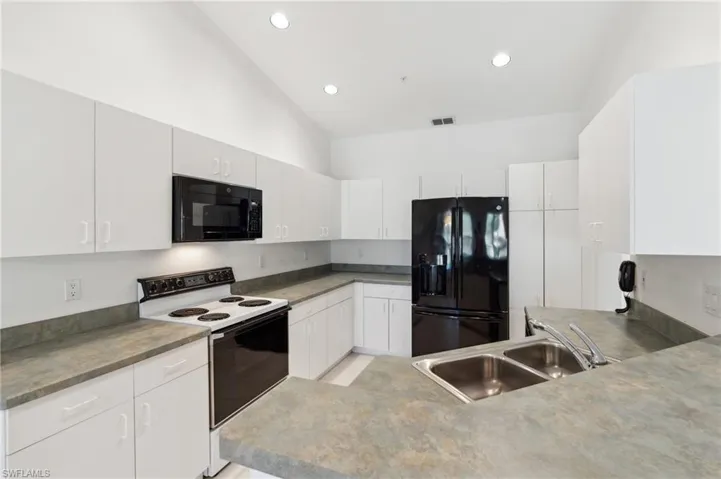 Kitchen featuring black appliances, a sink, lofted ceiling, recessed lighting, and white cabinets