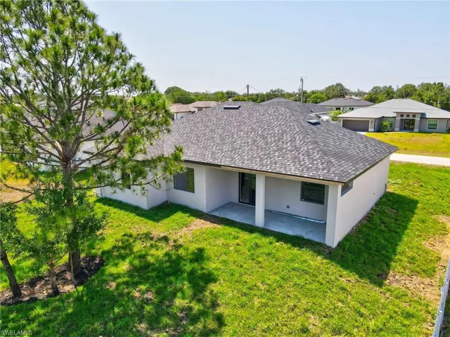 Rear view of house with a lawn, stucco siding, a patio, and a shingled roof