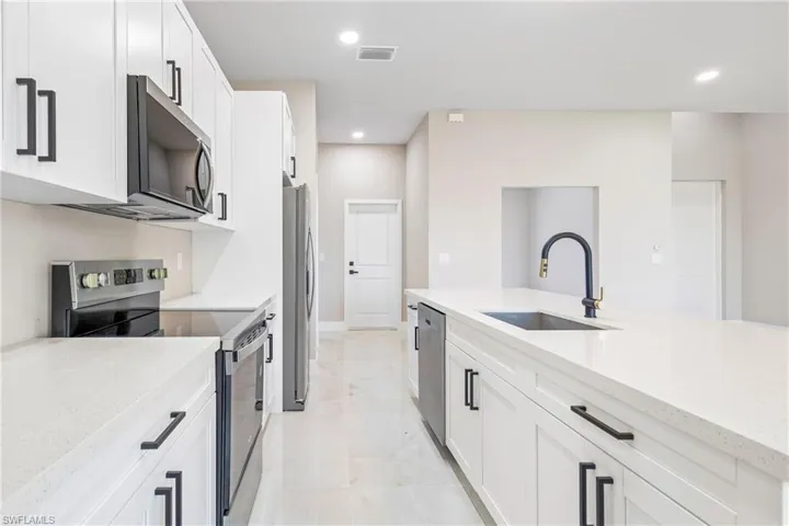 Kitchen featuring stainless steel appliances, white cabinets, light stone countertops, and recessed lighting