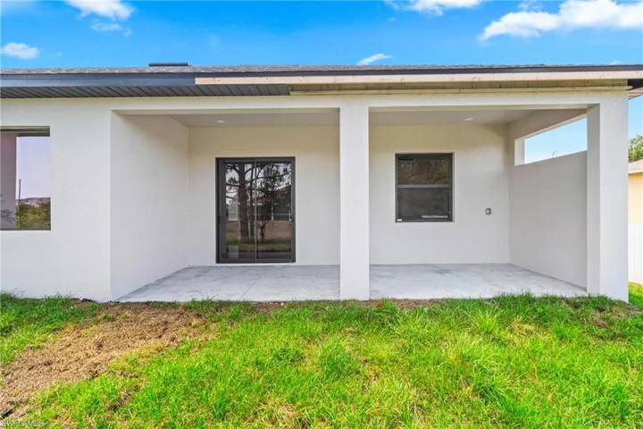 Doorway to property featuring stucco siding, a patio, and a lawn