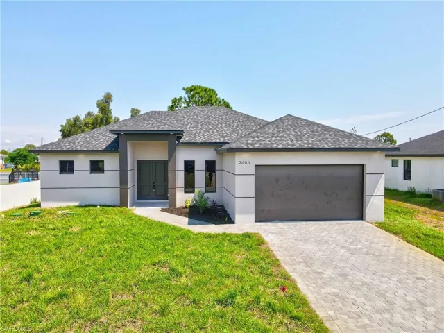 View of front facade featuring stucco siding, a front lawn, roof with shingles, driveway, and a garage