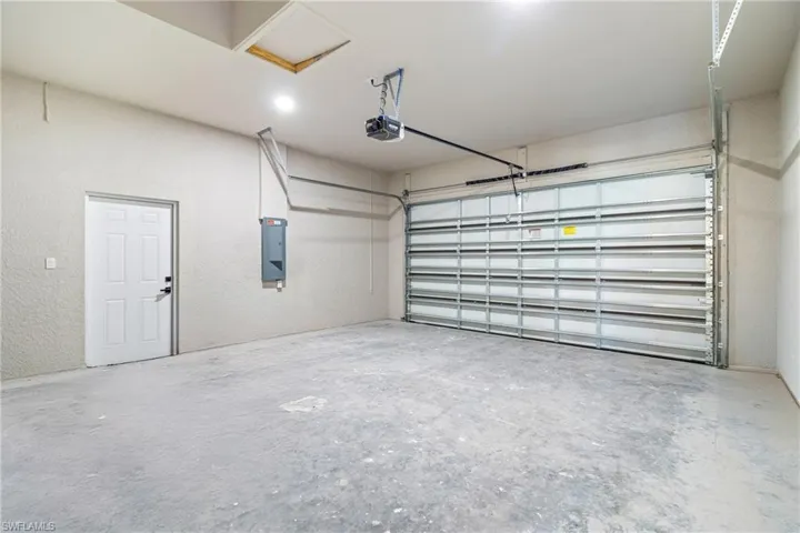 Garage with a textured wall, electric panel, and a garage door opener