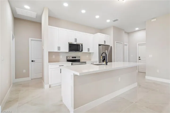 Kitchen with stainless steel appliances, white cabinetry, a center island with sink, recessed lighting, and light stone counters