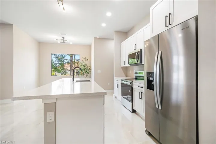 Kitchen featuring stainless steel appliances, white cabinetry, light stone counters, recessed lighting, and a center island with sink