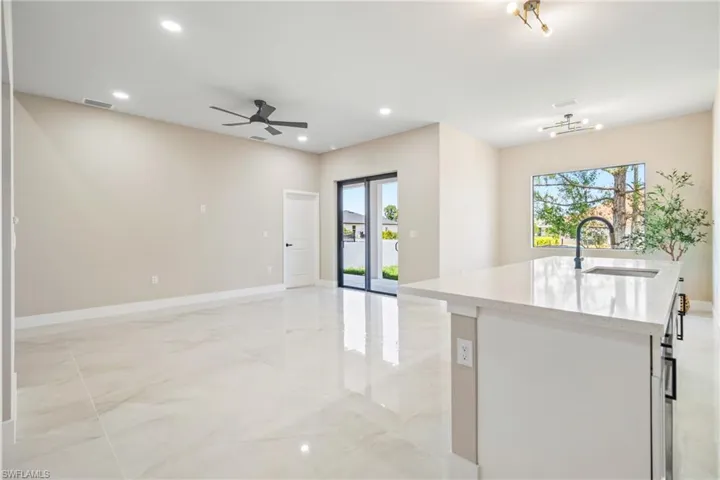 Kitchen featuring an island with sink, light stone counters, recessed lighting, a ceiling fan, and open floor plan