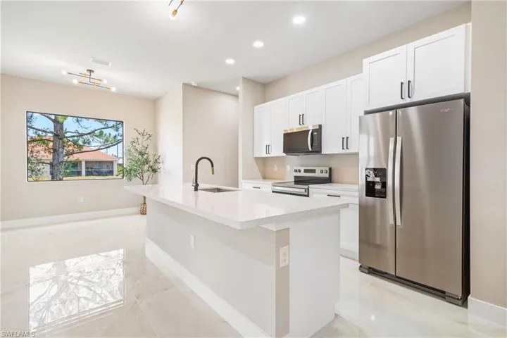Kitchen with stainless steel appliances, an island with sink, white cabinets, recessed lighting, and light stone countertops