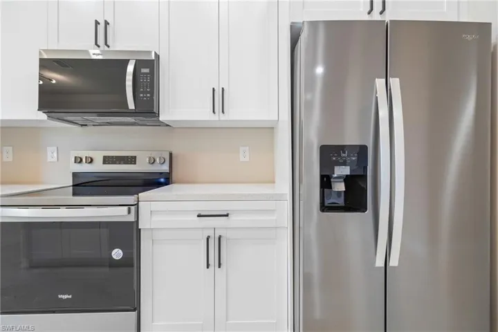 Kitchen with stainless steel appliances, white cabinets, and light stone countertops
