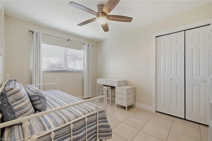 Room featuring tiled flooring, a window with blinds and drapes, a ceiling fan with integrated lighting, and a closet with bifold doors