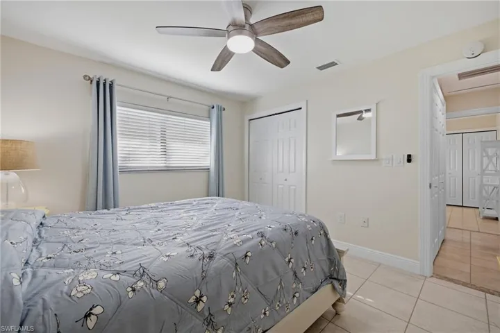 Bedroom featuring tile flooring, a window with horizontal blinds, a ceiling fan with light fixture, and bifold closet doors