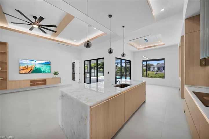 Open-concept living space featuring a waterfall island with a sink, light wood-finish cabinetry, and white tile flooring