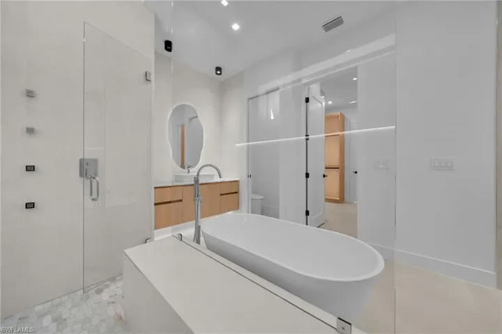 Contemporary bathroom featuring a freestanding soaking tub, a frameless glass shower enclosure with multiple showerheads, a wood-finish floating vanity with a vessel sink, and overhead recessed lighting