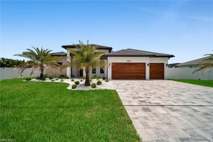 Contemporary architectural style featuring a two-car garage with wood-finish doors, a paver driveway, and a tile roof