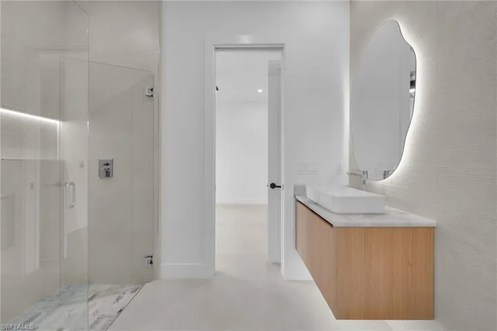 Modern bathroom featuring a floating wood-finish vanity with a rectangular vessel sink, a backlit organic-shaped mirror, and a glass-enclosed shower with tile flooring