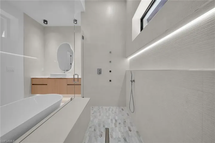 Spa-inspired bathroom featuring a freestanding soaking tub, frameless glass shower enclosure, wood-finish floating vanity with vessel sink, and textured tile shower walls with integrated lighting
