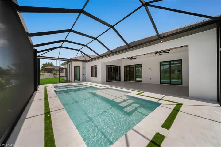 Screened lanai featuring a swimming pool, integrated spa, and expansive patio with tile flooring and artificial turf accents