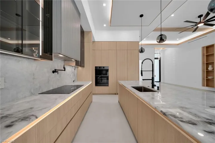 Modern kitchen featuring light wood-finish cabinetry, integrated appliances, and stone countertops