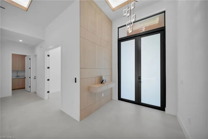 Entryway featuring a double-door entrance with transom window, a prominent wood-panel accent wall with built-in floating console, and a contemporary chandelier