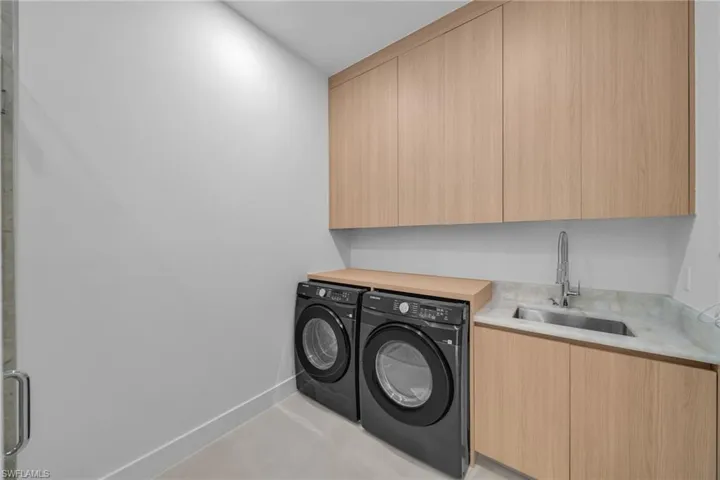 Laundry area featuring light wood-finish cabinetry, a stainless steel sink with a chrome faucet, and a stone-finish countertop