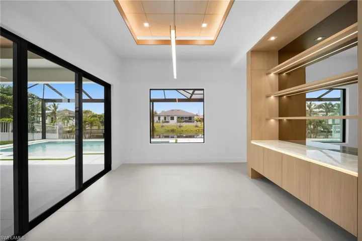 Spacious interior featuring large format tile flooring and a built-in wood-finish cabinet with illuminated shelving and a stone countertop