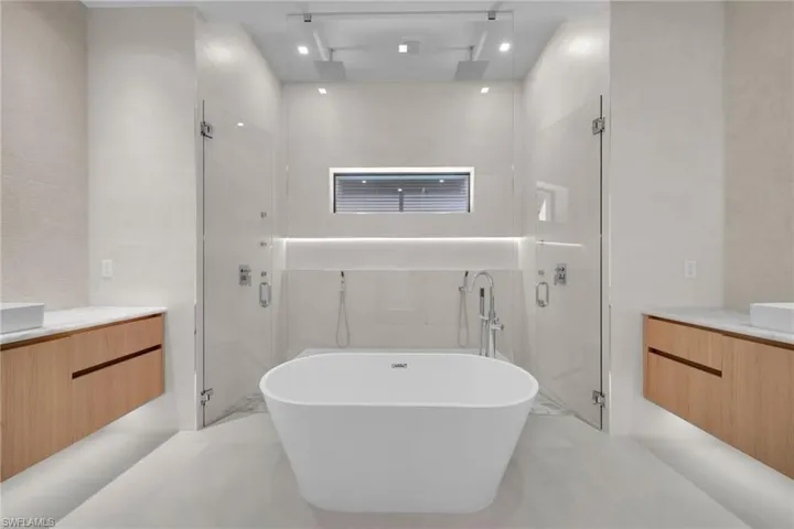 Freestanding soaking tub centered between two glass-enclosed shower spaces
