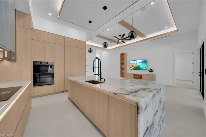 Gourmet kitchen featuring a waterfall island with a stone surface, integrated sink, and modern black faucet