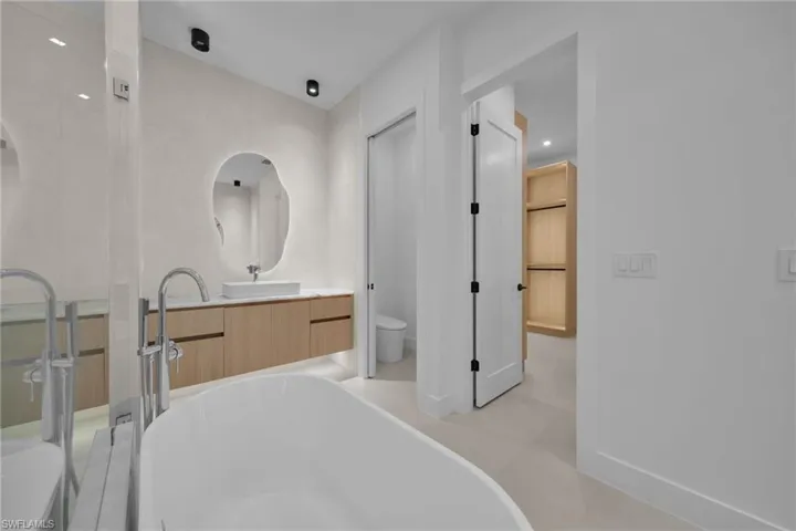 Contemporary bathroom featuring a freestanding tub, floating wood-finish vanity with countertop vessel sink, and an irregular shaped mirror
