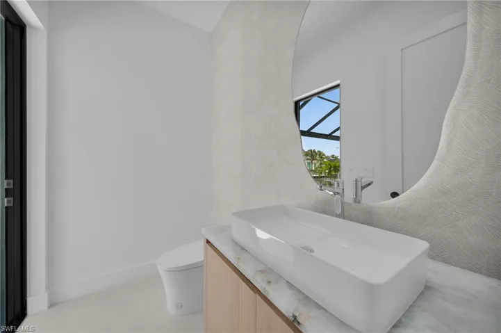 Contemporary bathroom featuring a rectangular vessel sink, polished chrome faucet, light wood-finish vanity with stone countertop, and a uniquely shaped mirror with patterned detailing