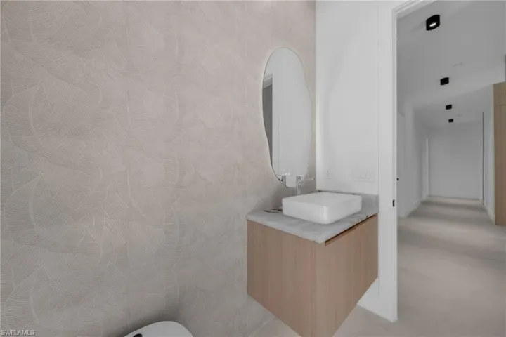 Modern powder room featuring textured accent wallpaper, a floating wood-finish vanity with a vessel sink, a stone countertop, and an illuminated oval mirror