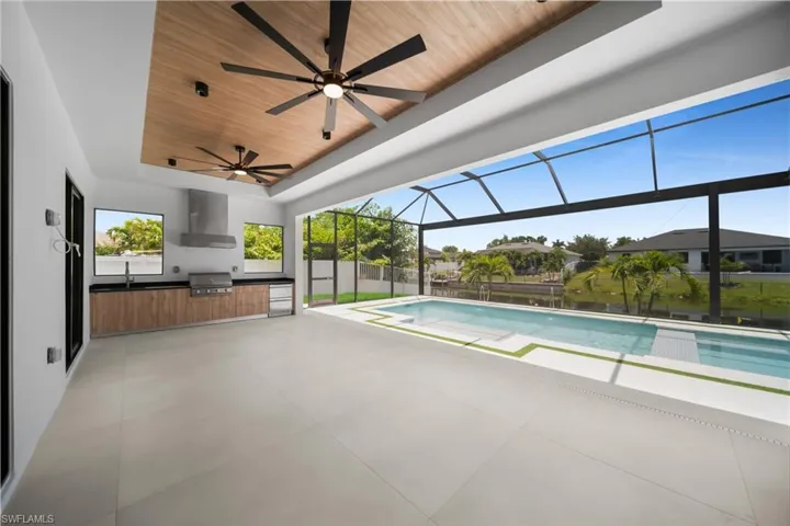 Expansive covered patio featuring a full outdoor kitchen, two ceiling fans, and a screened swimming pool