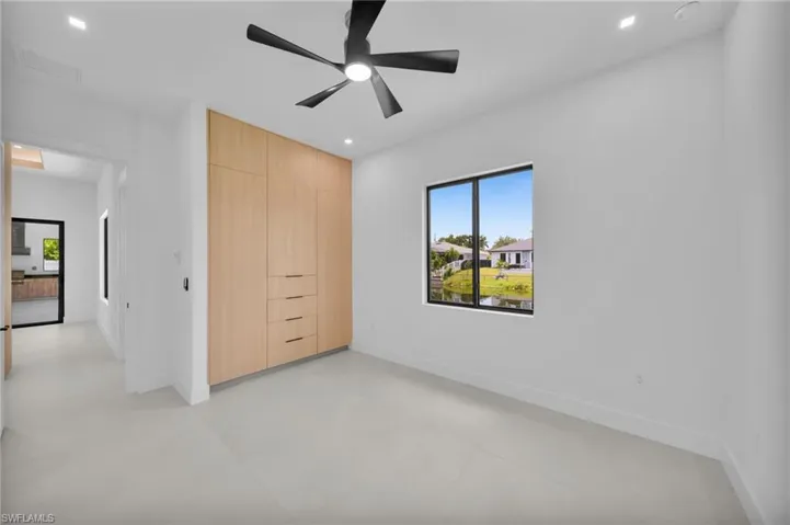 Room featuring a large window, light wood-finish built-in cabinetry with drawers, light tile flooring, a black ceiling fan, and recessed lighting