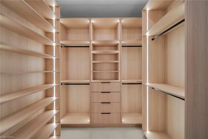 Custom closet system featuring light wood-finish cabinetry, integrated strip lighting, multiple shelving units, hanging rods, and built-in drawers with dark hardware