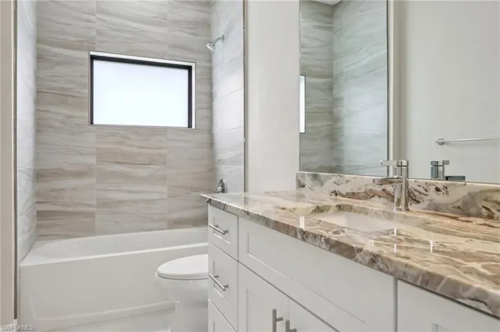Guest bathroom- tiled shower and tub combo with granite countertops.